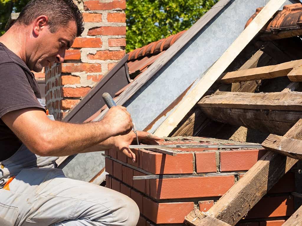 Chimney repair image man on roof with bricks